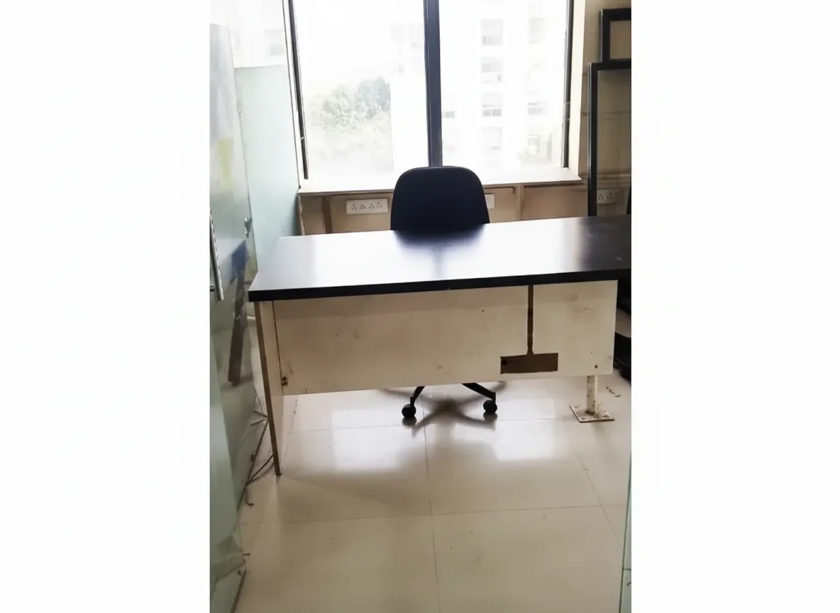 Bright cabin in office on rent on Ashram Road: Black-top wooden desk, white base, black swivel chair, frosted glass partition, large window with blinds, tiled floor. Ideal for solo professional.